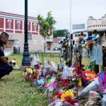 Midnight Massacre – 6 SHOT, 2 Kids! Police officer kneels at a memorial with flowers and tributes.