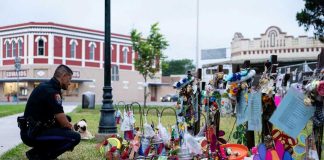 Midnight Massacre – 6 SHOT, 2 Kids! Police officer kneels at a memorial with flowers and tributes.