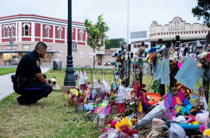 Police officer kneels at a memorial with flowers and tributes.