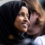 Ilhan Omar BROKE – Millionaire Mirage Explodes! A woman wearing a black hijab smiling at an outdoor event