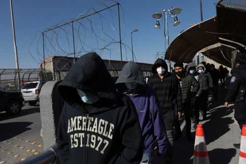 People in hoodies and masks walking beside a fence.