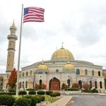 Lt. Governor Targets Mosques’ Loudspeakers A mosque with a golden dome and minarets, featuring an American flag in front