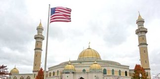 A mosque with a golden dome and minarets, featuring an American flag in front