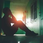 Person sitting on hallway floor with head in hands at sunset