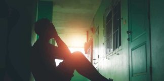 Person sitting on hallway floor with head in hands at sunset