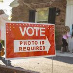 Red voting sign with arrow near people entering a polling place