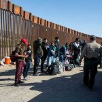 Trump Warns U.S Invasion Bigger Than Spain Group of people standing by a border fence with officers and vehicles