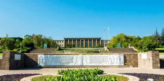Government building behind landscaped gardens and a stone relief wall