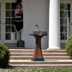 Taxpayer-Funded Trump Ad Sparks Uproar Podium with presidential seal in a garden colonnade