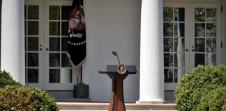 Taxpayer-Funded Trump Ad Sparks Uproar Podium with presidential seal in a garden colonnade