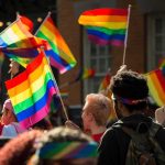 Crowd waving rainbow flags at an outdoor event