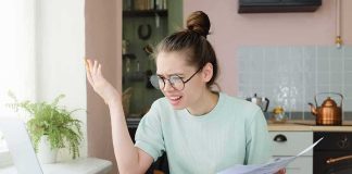 Young woman with glasses frustrated at laptop while holding bills