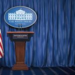 White House press briefing podium with U.S. flag and blue curtain
