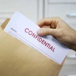 Hand placing confidential document into a brown envelope