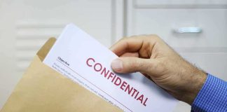 Hand placing confidential document into a brown envelope