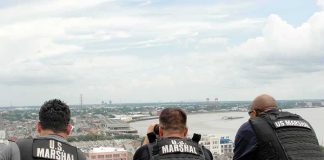 Three U.S. Marshals in tactical vests overlooking a city and river