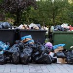 Overflowing dumpsters with piles of trash bags and cardboard