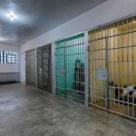 Arrested Cop Found DEAD Inside Prison Cell Interior view of a prison cell block with metal bars and concrete flooring