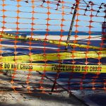 Orange safety net and yellow police tape blocking a beach access
