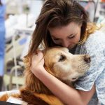 Patient in hospital gown hugging a golden retriever