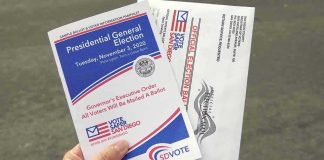 Hand holding election pamphlet and mail-in ballot envelopes