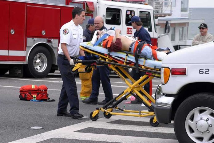 shutterstock_202643 Gary Patterson on a stretcher being moved by paramedics near fire trucks and an ambulance