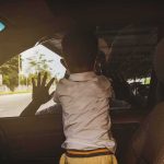 Child leaning on car window from the back seat