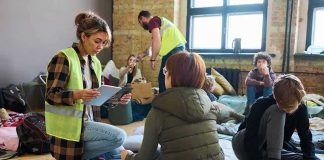 Volunteers assist people resting on mats in a temporary shelter