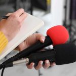 Pizza Standoff Ignites – Servicemen DENIED! Journalist holding two microphones while writing in a notebook