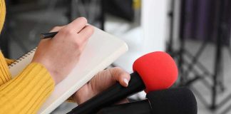 Journalist holding two microphones while writing in a notebook