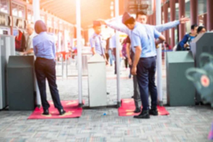 shutterstock_685297528 Security officers screen people at walk-through metal detectors