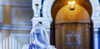 El-Sayed’s ‘Lesbian Rosh Hashanah’ Stunt BACKFIRES Spectacularly Person in white and blue prayer shawl facing ornate interior