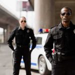 Two police officers standing by a patrol car under an overpass