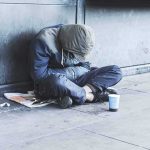 Person sitting on a sidewalk with head down and hood up