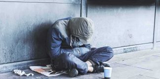 Person sitting on a sidewalk with head down and hood up
