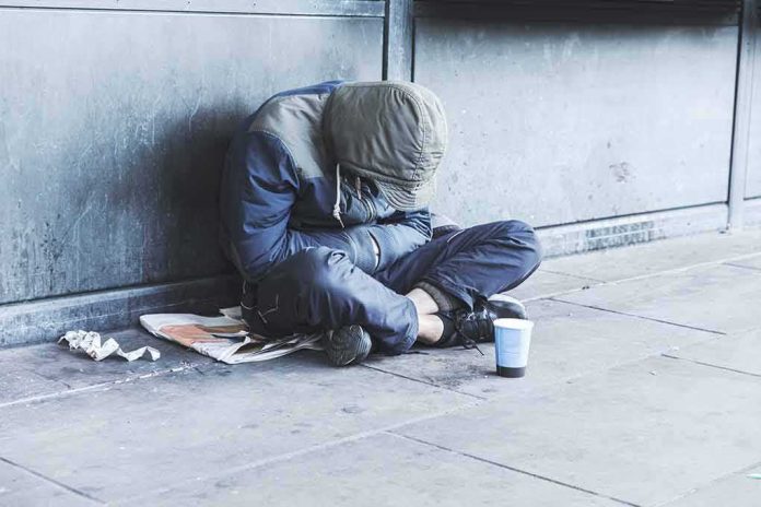shutterstock_1155406366 Person sitting on a sidewalk with head down and hood up