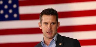 man speaking in front of a large American flag