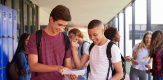 Two students smiling and comparing papers in a school hallway